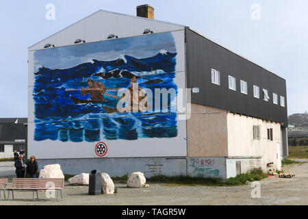 Tourists standing next to a mural depicting native kayakers on a building in the village of Paamiut on the west coast of Greenland. Stock Photo