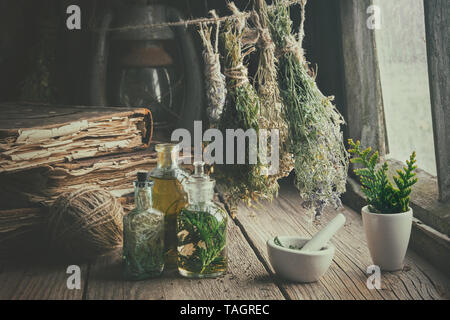 Infusion bottles, old books, mortar and hanging bunches of dry medicinal herbs. Herbal medicine. Retro styled. Stock Photo