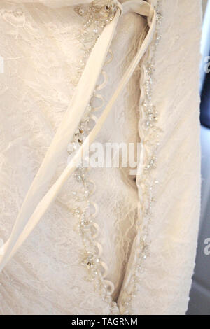 The back side of a beautiful ivory colored wedding gown being laced up with a long ribbon Stock Photo