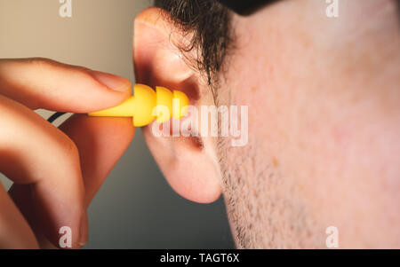 Man worker inserting yellow hearing safety protection earplug in his ear close-up view Stock Photo