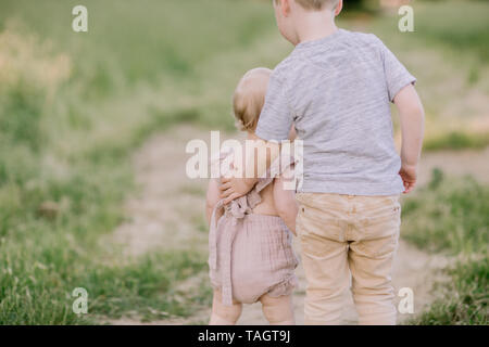 big brother and baby sister hug in a field Stock Photo
