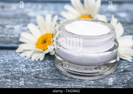 Cosmetic cream in a glass jar stands near chamomile flowers. Stock Photo