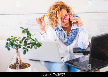 People at work and job stress concept with woman business manager speaking at the phone and work on two different computer table on the desk - busy la Stock Photo