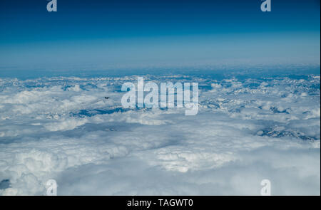 Small figure of an airplane. White heavy clouds in the blue sky. Panoramic cloudscape above the clouds. Stock Photo