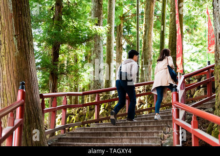 Nikko, Japan - April 4, 2019: Couple tourists walking on red railing stone steps stairs up in Tochigi prefecture in mountain forest leading to Toshogu Stock Photo