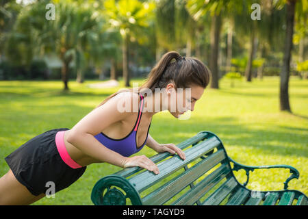 Woman doing bench push-ups exercise in the park during her fitness workout Stock Photo