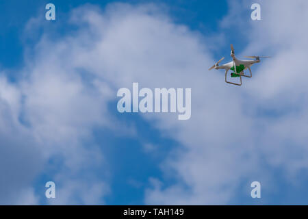 Flying white drone with a green camera on the background of blurred blue sky with clouds. Photo, video or patrol from a height. Stock Photo