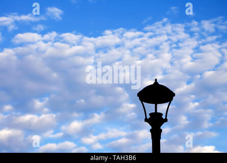 Silhouette of a street lamp missing a bulb among a bright cloudy day. Stock Photo