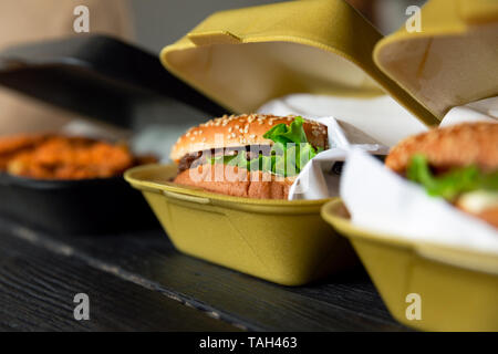 Hamburger in a takeaway container on the wooden background. Food delivery and fast food concept Stock Photo
