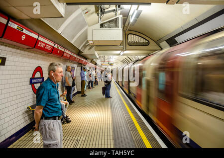 A train pulls into Bond Street London Underground Railway Station on the Central Line as passengers stand and wait on the platform. Stock Photo