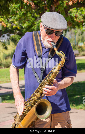 Old Man Playing Jazz trying to earn some money in the park. Stock Photo