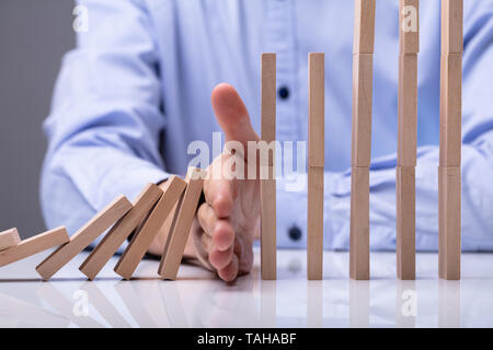 Close-up Of A Businessman Stopping Wooden Blocks With His Finger From Falling On Reflective Desk Stock Photo