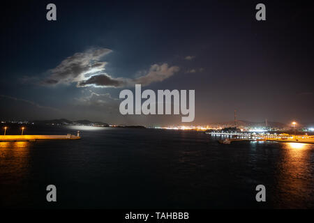 Night view of Athens Piraeus harbor with moon partially hidden by clouds, Greece Stock Photo
