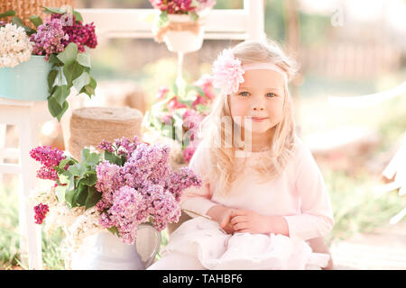 Smiling kid girl 4-5 year old posing with flowers outdoors. Summer time. Stock Photo