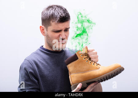 Close-up Of A Young Man Holding Stinky Shoes Against White Background Stock Photo