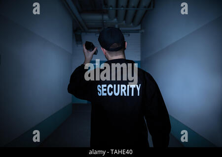 Rear View Of A Male Security Guard With Flashlight Standing In Corridor Stock Photo