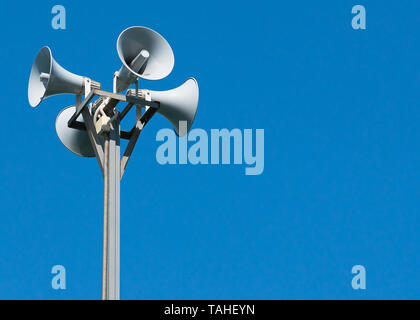 A tall column with four gray loudspeakers in a circle against a clean blue sky. Hazard warning system. The possibility of placing your test or image. Stock Photo