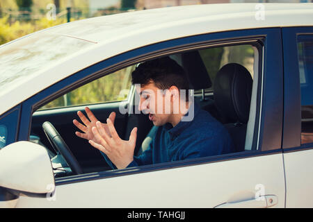Angry man driving a vehicle arguing and gesturing shaking his hands perplexed. Irritated and furious guy negative facial expression, while driving the Stock Photo
