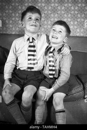 Family Life in the UK c1950  Two young brothers looking happy on a settee in school uniform  Photo by Tony Henshaw Stock Photo