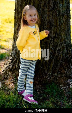 Little girl leaning laughing against a tree trunk, Czech Republic Stock Photo