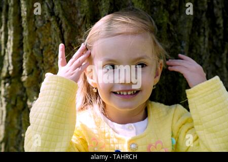 Portrait, little laughing girl brushing hair from her face, Czech Republic Stock Photo