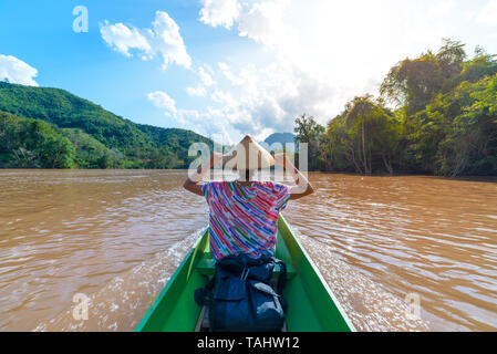 Woman with traditional hat cruising on the brown water of the Nam Ou river in Laos, amazing landscape mountain jungle famous travel destination in Sou Stock Photo