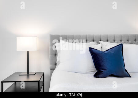 A bedroom detail shot with white bedding, blue pillow, and a lamp on the bedside table. Stock Photo