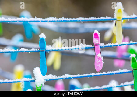 Snow covered plastic clothes pegs on rotary washing line Stock Photo