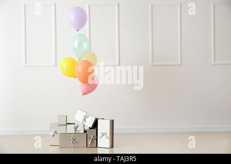 Colorful balloons and gift boxes on floor against light wall Stock Photo