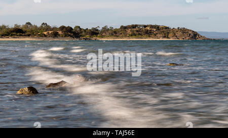 Wave Breaking Over Rocks, Motion Blur, Beach in Background Stock Photo