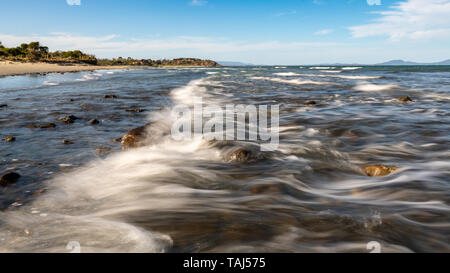 Wave Breaking Over Rocks, Motion Blur, Beach in Background Stock Photo