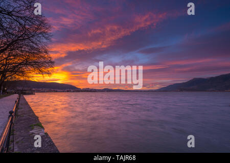 Vivid sunset along the lake promenade in Ioannina, Greece. Dramatic colours in the sky for sunset along the waterfront. Stock Photo