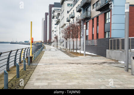 View of a Riverside footpath lined with modern apartment buildings on a cloudy winter day. Glasgow, Scotland, UK. Stock Photo