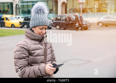 Woman using her smartphone while walking in a city centre on a cold winter day Stock Photo