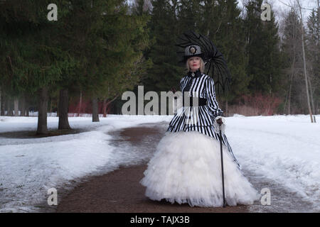 elderly woman in a gothic dress in a hat with a black umbrella on nature in winter Stock Photo