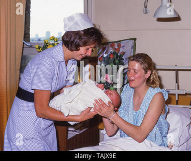 Midwife handing baby to young mother in maternity ward in private hospital, Greater London, England, United Kingdom Stock Photo