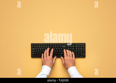 Top view of male hands typing on black computer keyboard over yellow background. Stock Photo