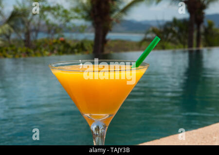 Mango margarita beside a pool with palm trees and the ocean in the background Stock Photo