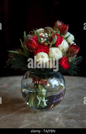 Spring bouquet of white ranunculus and red tulips in a glass round vase on a dark background, soft focus Stock Photo