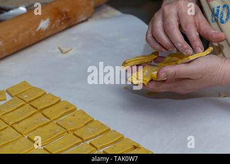 A woman placing cut dough for homemade southern chicken and dumplings in her hand before placing it in the cooking pot. Stock Photo