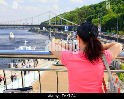 A young woman looks at the embankment of the Dnieper River in Kiev, Ukraine. A lady traveler in a bright pink T-shirt stands on the observation deck a Stock Photo