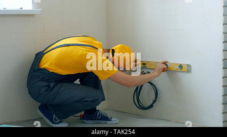 Young male builder with level tool. Construction worker checking measurements of interior wall with spirit level. Stock Photo