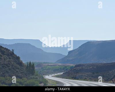 Virgin, Utah--July 2018: Winding road with the faint silhouettes of distant mountains Zion National Park in the late afternoon sun. Stock Photo