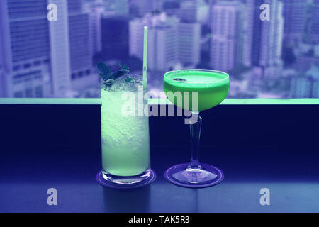 Two different type of cocktails in vibrant green color on the rooftop bar's table with blurry skyscrapers view in background Stock Photo
