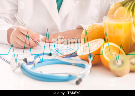 Dietitian doctor writing a diet list with fruit on a desk Stock Photo