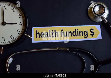 Health Funding $ on the print paper with Healthcare Concept Inspiration. alarm clock, Black stethoscope. Stock Photo