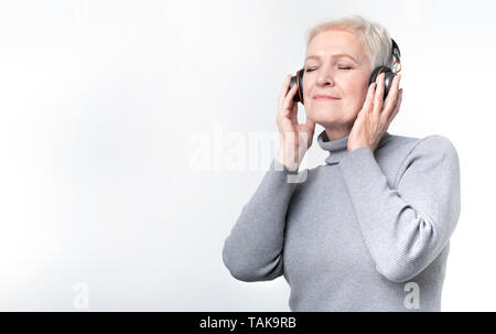 Senior woman listening to music in wireless headphones Stock Photo