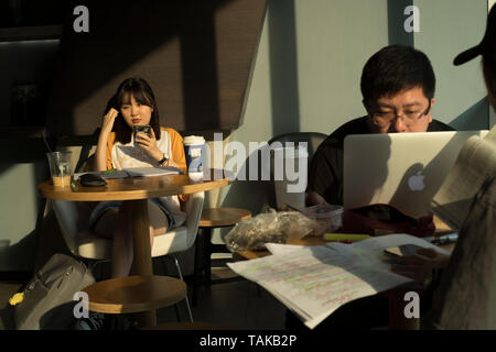 Chinese young man and woman using the digital tablet in a coffee shop in Beijing, China. 25-May-2019 Stock Photo