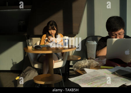 Chinese young man and woman using the digital tablet in a coffee shop in Beijing, China. 25-May-2019 Stock Photo