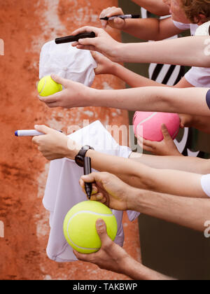 Tennis fans extending hands to offer balls and hats to get an autograph from tennis player after win, closeup photo showing hands waiting for player s Stock Photo